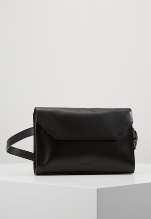 Sac bandoulière rectangulaire en cuir noir avec fermeture à rabat et sangle réglable, présenté sur un socle blanc devant un fond gris.