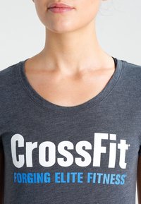 Šedé bavlněné tričko s kulatým výstřihem a krátkými rukávy, s bílým a modrým nápisem "CrossFit FORGING ELITE FITNESS."