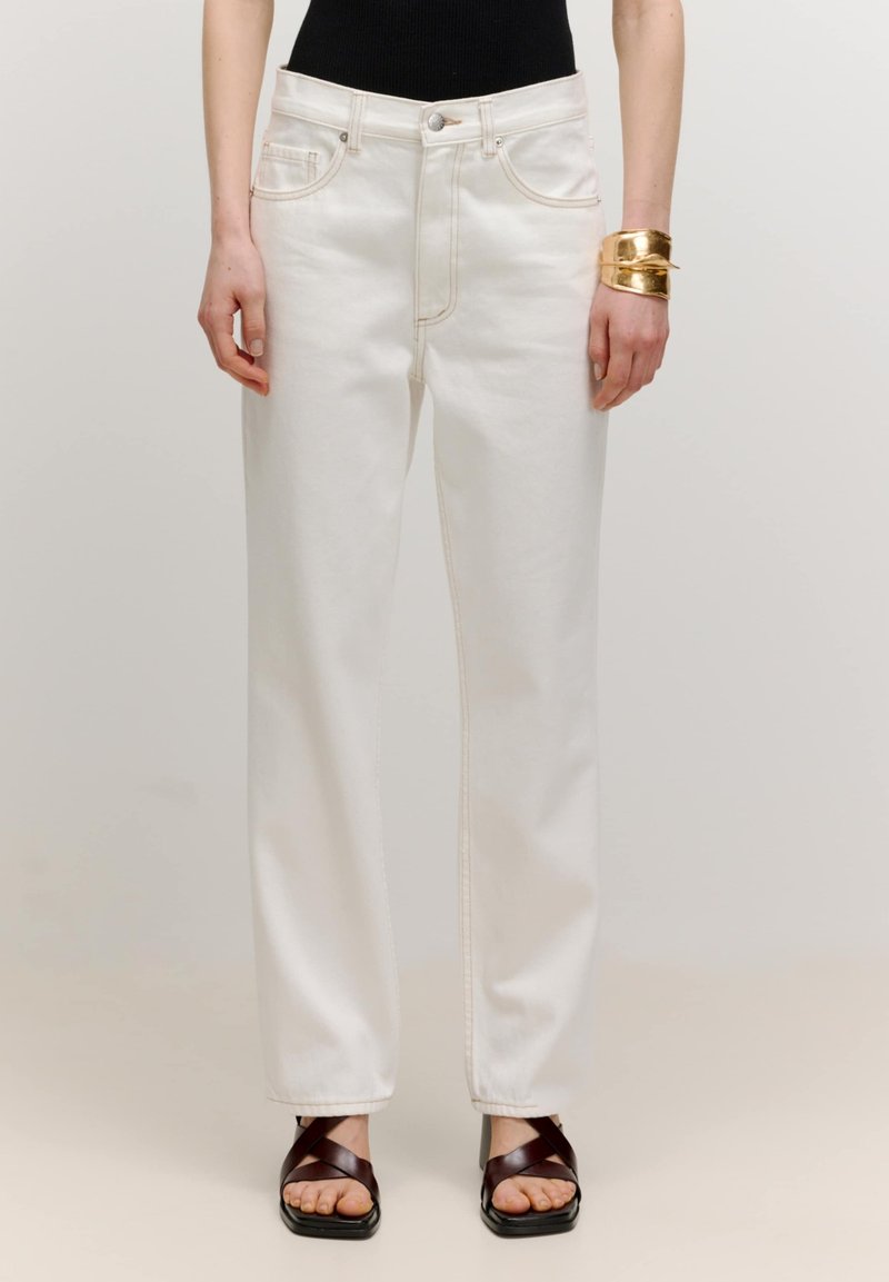 Weiße weite Jeans mit kontrastierenden Nähten, fünf Taschen und einem Knopfverschluss, kombiniert mit braunen Riemchensandalen.
