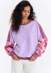 Lilla dressipluus roosade ja oranžide lillemustritega varrukatega, ümar kaelus ja soonikkoes varrukasääred. Pehme tekstuur, vaba lõige.