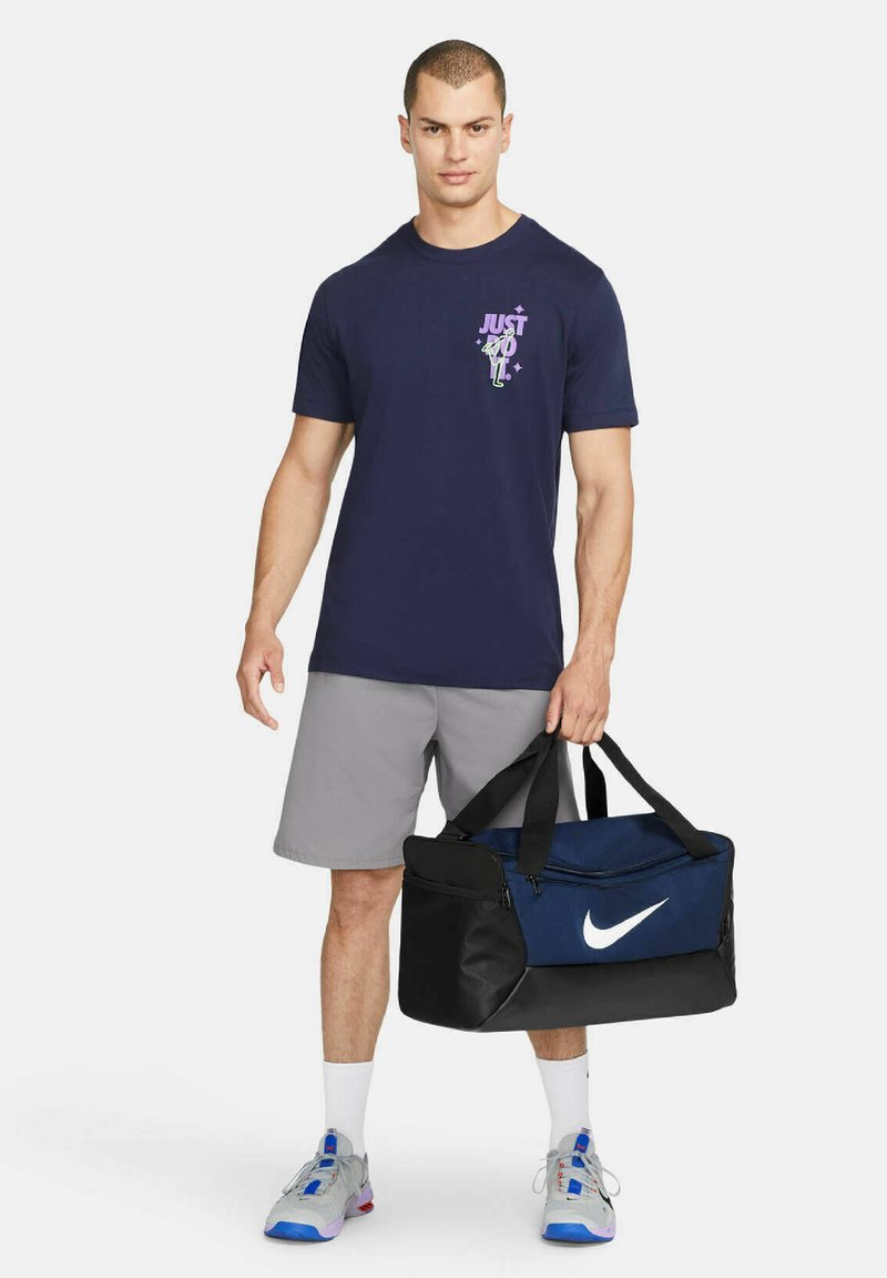 T-shirt graphique marine avec le design "Just Do It" ; shorts gris ; sac de sport noir et marine ; chaussures grises avec des accents bleus ; design minimaliste.