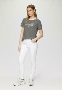 Grijs en wit gestreept T-shirt met korte mouwen met de tekst "zonlicht", gecombineerd met witte slim-fit jeans en lichtgrijze sneakers.