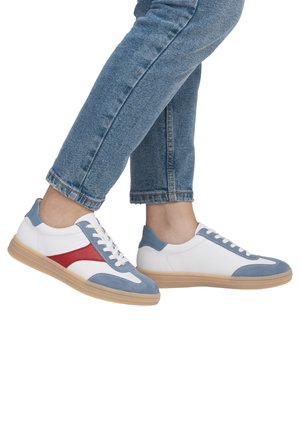 Des baskets blanches avec des accents en suède bleu clair et rouge, une semelle en caoutchouc texturée, des lacets plats et un embout arrondi, portées avec un jean en denim.