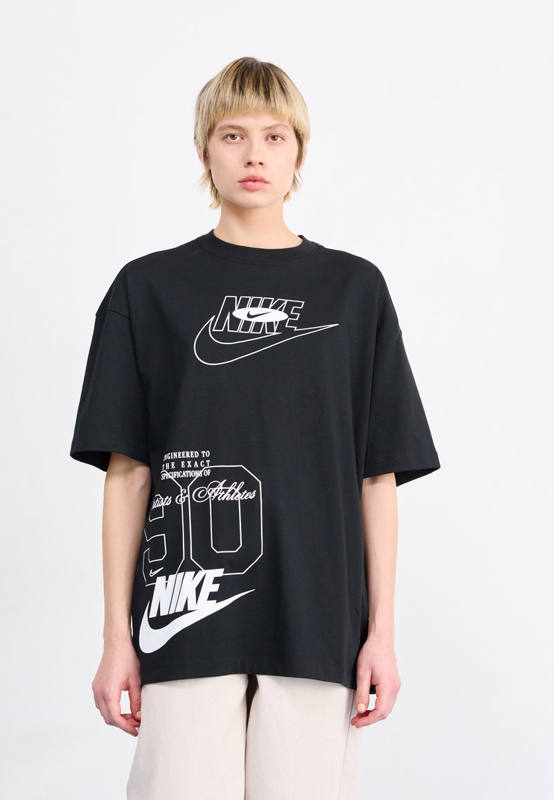 Juodas oversized Nike marškinėliai su baltais grafikos logotipais ir tekstu, apvaliu iškirpimu ir trumpomis rankovėmis. Laisvas siluetas, medvilnės audinys.