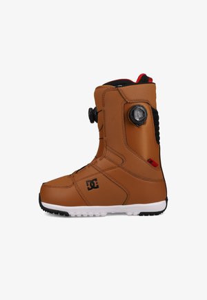 Bruine snowboardboot met een gestructureerd oppervlak, zwarte accenten, een cirkelvormige draaiknop voor het aanspannen en een contrasterende witte zool.