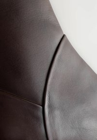Rivestimento in pelle marrone con una texture liscia, caratterizzato da cuciture curve e sottili venature, che conferisce un aspetto moderno e snello.