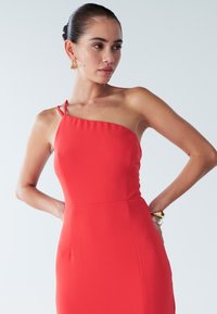 Punainen, vartalonmyötäinen mekko, jossa on yksivartaloinen olkaimisto ja ohuet hihnat. Valmistettu sileästä kankaasta, tyylikkäällä siluetilla ja hienovaraisella sivutaskulla.