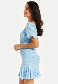 Light blue dress made of textured fabric with puff sleeves, dotted pattern, and a flared hem. The design features a fitted silhouette.