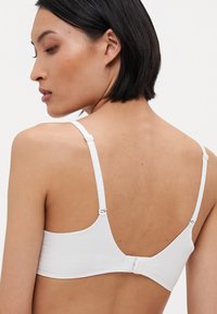 White bra with adjustable straps, smooth material, and a hook-and-eye back closure. Simple design with a clean, minimalist aesthetic.