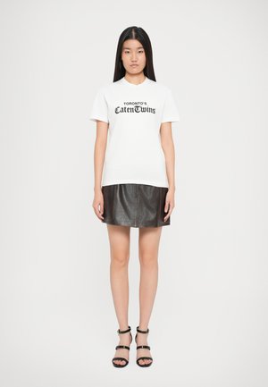 Hvid t-shirt med kortærmer, der har sort trykt tekst, parret med en mørkebrun lædernederdel med synlige sømme og en udskåret form.