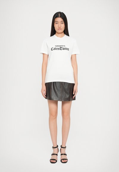 Weißes Kurzarm-T-Shirt mit schwarzem Drucktext, kombiniert mit einem dunkelbraunen Lederrock mit sichtbaren Nähten und einer ausgestellten Form.