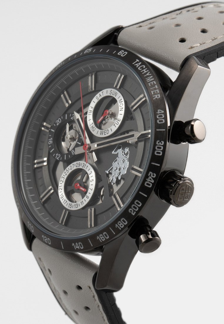 Montre chronographe avec un boîtier en métal noir, un cadran gris et des accents argentés. Dispose de trois sous-cadrans et d'un bracelet en cuir gris perforé.