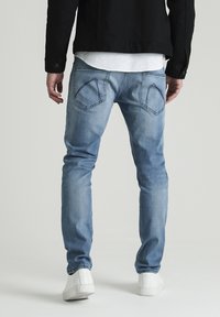 Světlé modré džíny z denimu s úzkým střihem, s charakteristickými kapsami na zadní straně ve tvaru diamantu a jemným vyblednutím, doplněné bílými botami.