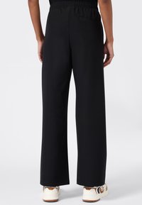 Zwarte, wijde broek met een gladde textuur en elastische tailleband; heeft een enkele achterzak en subtiele stikdetails.