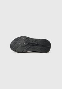 Semelle de chaussure en caoutchouc noir avec des motifs texturés et des rainures pour une meilleure adhérence. Accent notable comprenant un logo en relief au centre.