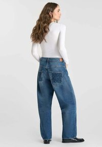 Blauwe denim oversized broek met een hoge taille, twee achterzakken met een patroon en zwarte laarzen. Soepele textuur, relaxte pasvorm.