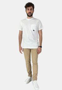 T-shirt bianca con taschino sul petto, pantaloni beige chiaro e sneakers bianche. Vestibilità casual, materiale di cotone e dettagli di design minimal.