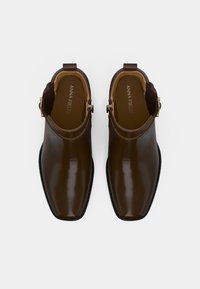 Par de botas de cuero marrón oscuro hasta el tobillo con puntas cuadradas y hebillas doradas, mostradas desde arriba sobre un fondo blanco.