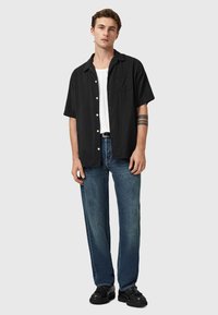 Kortærmet sort skjorte med lodrette striber, hvid tanktop, blå jeans og sorte sko. Pyntet med en brystlomme og knapper.