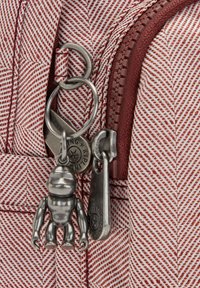 Tessuto a righe rosse e bianche con una tasca con zip, dotato di hardware in metallo argentato per portachiavi e una piccola figura giocattolo metallica attaccata.