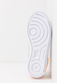 Bílá podrážka tenisky s kruhovými a vlnitými vzory, texturovaným gripem a oranžovým akcentem na patě; mírně zakřivený tvar.