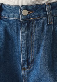 Modré džínové kalhoty s vysokým pasem, s oranžovým prošitím, kovovým knoflíkem a jemným vyblednutím. Hladká textura, klasický design.