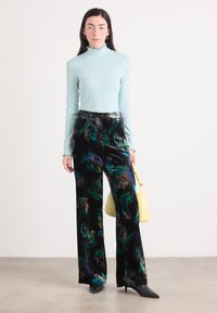 Top lung cu mâneci lungi de culoare bleu deschis, cu decolteu răsfrânt; pantaloni din catifea neagră cu modele colorate de frunze; geantă galbenă; pantofi ascuțiți negri.