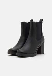 Botine negre din piele cu un aspect neted, panouri elastice pe laterale și un toc chunky înalt. Dispune de un design minimalist și un tab de prindere.