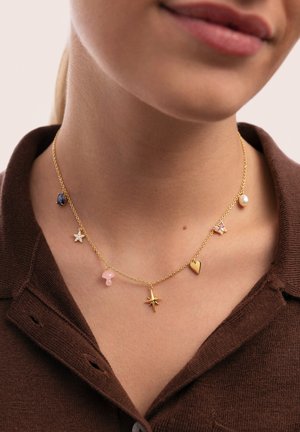 Collar de cadena dorada con siete colgantes que incluyen estrellas, un corazón, un hongo rosa y una perla, con una mezcla de texturas y colores.