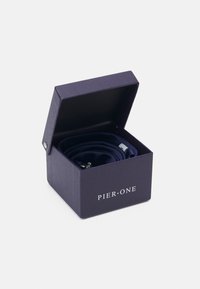 Boîte violette avec un couvercle présentant un matériau noir enroulé à l'intérieur, sécurisé par du matériel en argent, marqué "PIER • ONE" à l'avant.