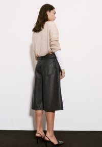 Culottes negre din piele au o croială lejeră, lungime până la glezne și buzunare la spate. Asortate cu un pulover bej din lână moale și pantofi cu toc negri.