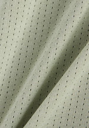 Hellgrüner Stoff mit gleichmäßig verteilten kleinen Perforationen und sichtbarer Strickstruktur, gezeigt in sanften Falten.