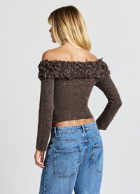 Pull marron à col bateau texturé et duveteux. Corps ajusté et manches longues, associé à un jean en denim bleu taille haute.