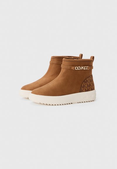 Braune Wildleder-Ankle Boots mit einer flachen, weißen Plattformsohle, die über einen dekorativen Riemen mit goldfarbenen Beschlägen und ein gemustertes Seitenpanel verfügen.