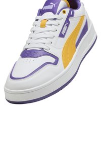 PUMA sneakers med en hvid læderoverdel med lilla og gule detaljer, en chunky sål og en perforeret tåboks for åndbarhed.