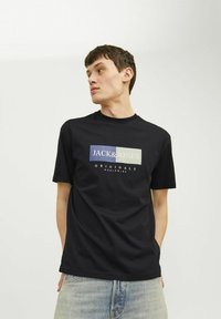 Melnas kokvilnas T-krekls ar ģeometrisku grafiku, kurā redzams "JACK & JONES" baltā un tonētā krāsā. Īsās piedurknes un apaļa kakla izgriezums.
