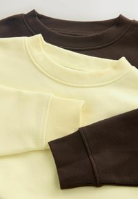 To sweatshirts, en gul og en brun, der overlapper hinanden. Begge har ribstrikkede halsudskæringer og manchetter. Den gule er blød, den brune er tekstureret.