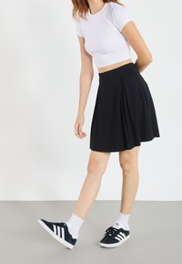 Zwarte geplooide rok met een aangesloten tailleband, gecombineerd met een wit crop top en zwarte sneakers met witte strepen. Soepele stof en een casual stijl.