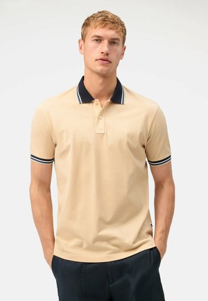 Polo beige avec col marine et accents rayés, à manches courtes et coupe ajustée. Tissu doux avec une texture côtelée.