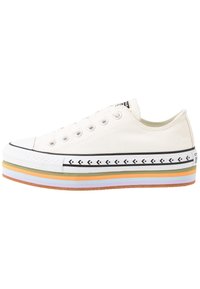 Canvas sneakers i off-white med rund tå, gummisula och flerfärgad lager-sula. Har ett svart pilmönster nära sulan.