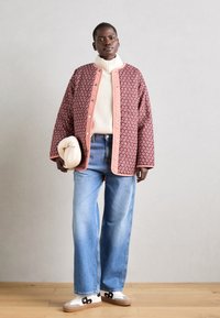 Röd mönstrad vadderad jacka med rosa detaljer, krämfärgad polotröja, ljusblå vida jeans och vita sneakers med svart design.