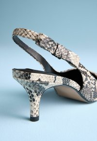 Pumps mit Absatz und offenem Fersenbereich im schwarz-creamfarbenen Schlangenprint. Mit einem geknoteten Riemen und einer strukturierten, glanzvollen Oberfläche.