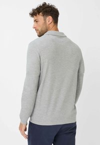 Graues Langarm-Polo-Shirt mit Kragen, gerippten Manschetten und strukturiertem Stoff. Modell wird von hinten betrachtet. Navy-Hosen sind sichtbar.