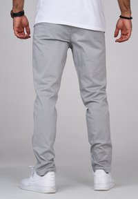 Ljust grå byxor med en slät yta, slim fit och ankellång design. Kombineras med vita sneakers med klassisk Nike-branding.