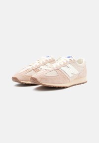 Ljusrosa sneakers i mocka med texturerad yta, vita detaljer och sula i gummi, med klassisk snörning och blå märkning.