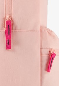 Sac à dos en tissu rose avec deux zippers, comportant des tirettes de fermeture éclair rose vif avec des accents noirs. Surface texturée, forme rectangulaire.