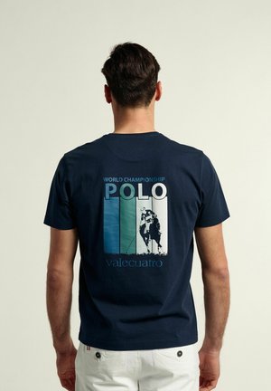 Camiseta de algodón azul marino con un gran gráfico en la parte posterior que presenta "CAMPEONATO MUNDIAL DE POLO" y una ilustración de un jugador de polo, impresión texturizada.