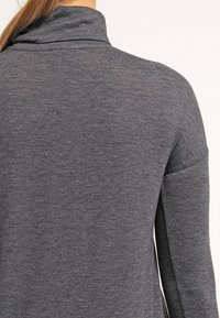 Maglione grigio antracite con colletto alto e maniche lunghe; presenta una texture morbida e lavorata a maglia. Design minimalista, senza motivi o hardware visibile.