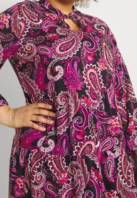 Vestido de manga larga en tejido negro con un estampado de cachemira en rosa. El diseño incluye un escote en forma de ojal y detalles de cintura fruncida.