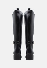 Botas de couro pretas até ao joelho com uma textura suave, zíperes laterais e um pequeno detalhe de fivela em cada panturrilha. Design de salto bloco.